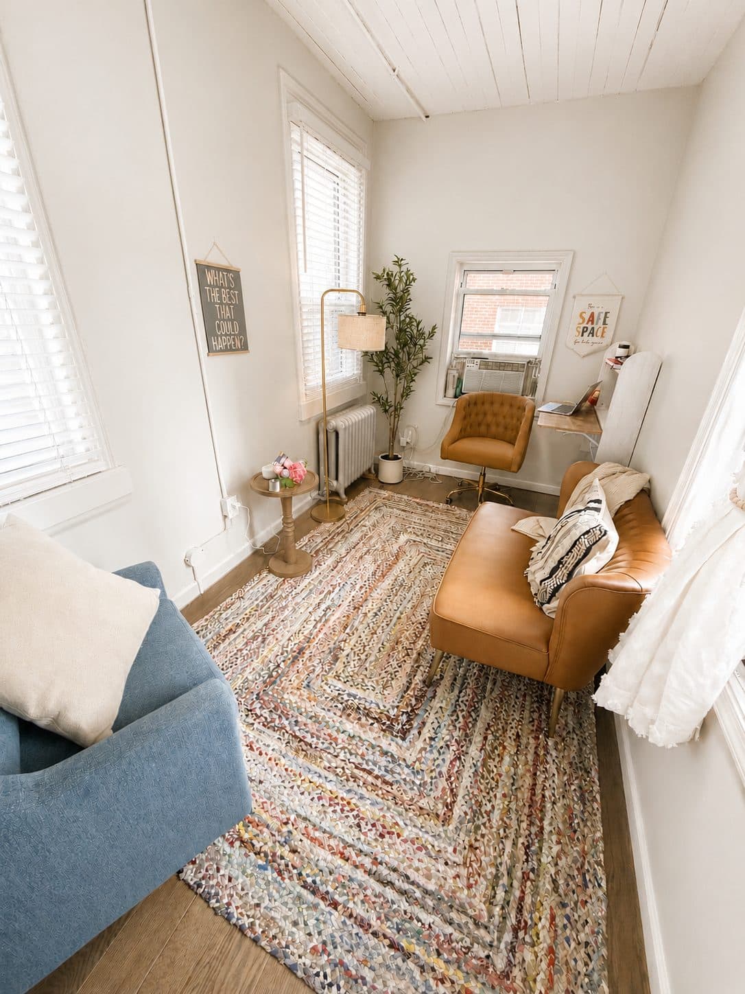 Everwell's therapy room: a tan leather sofa and blue armchair on a braided rug, with a plant beside a sunlit window.